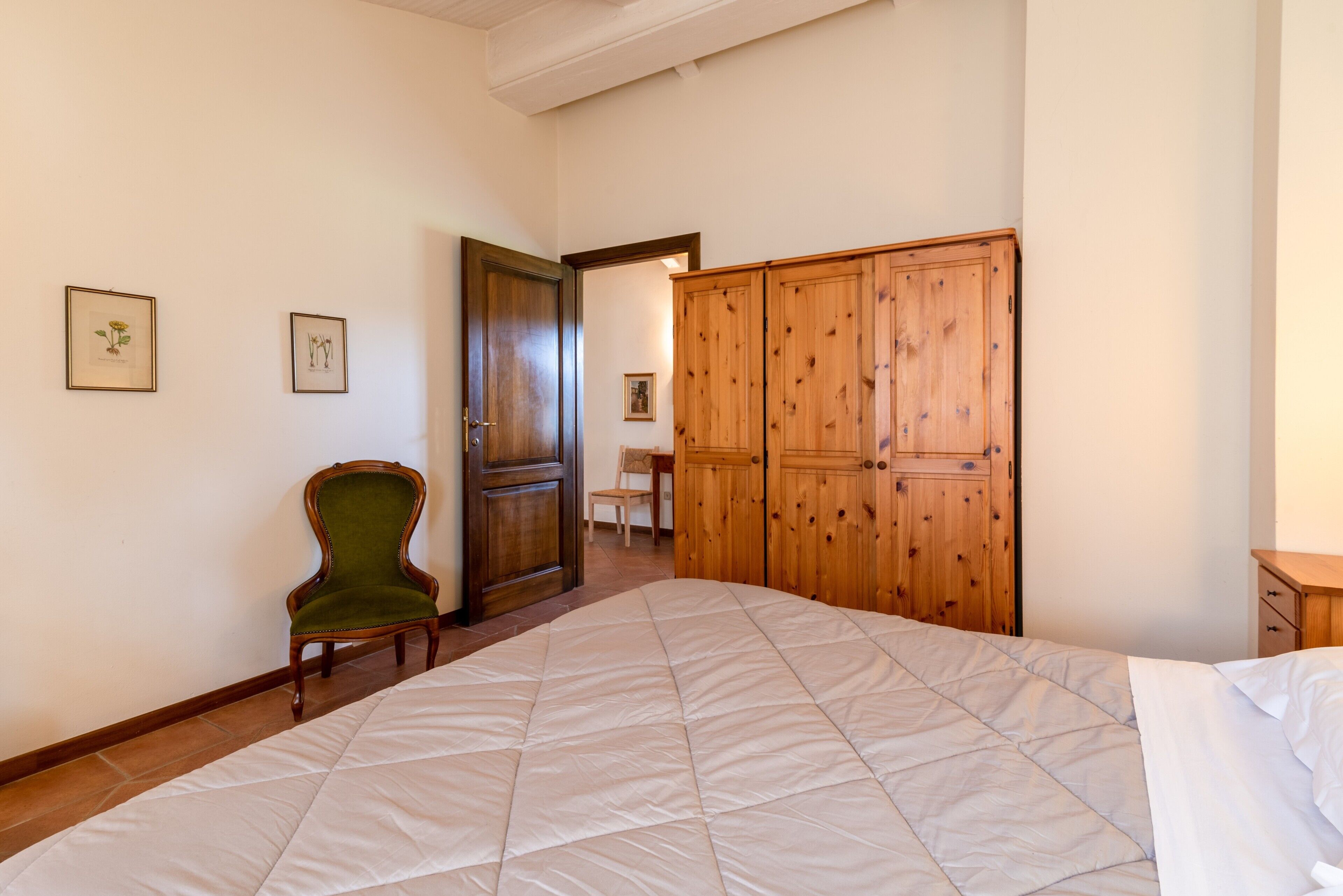 Una camera da letto con un letto grande, un'armadio in legno, una poltrona verde e quadri appesi al muro.