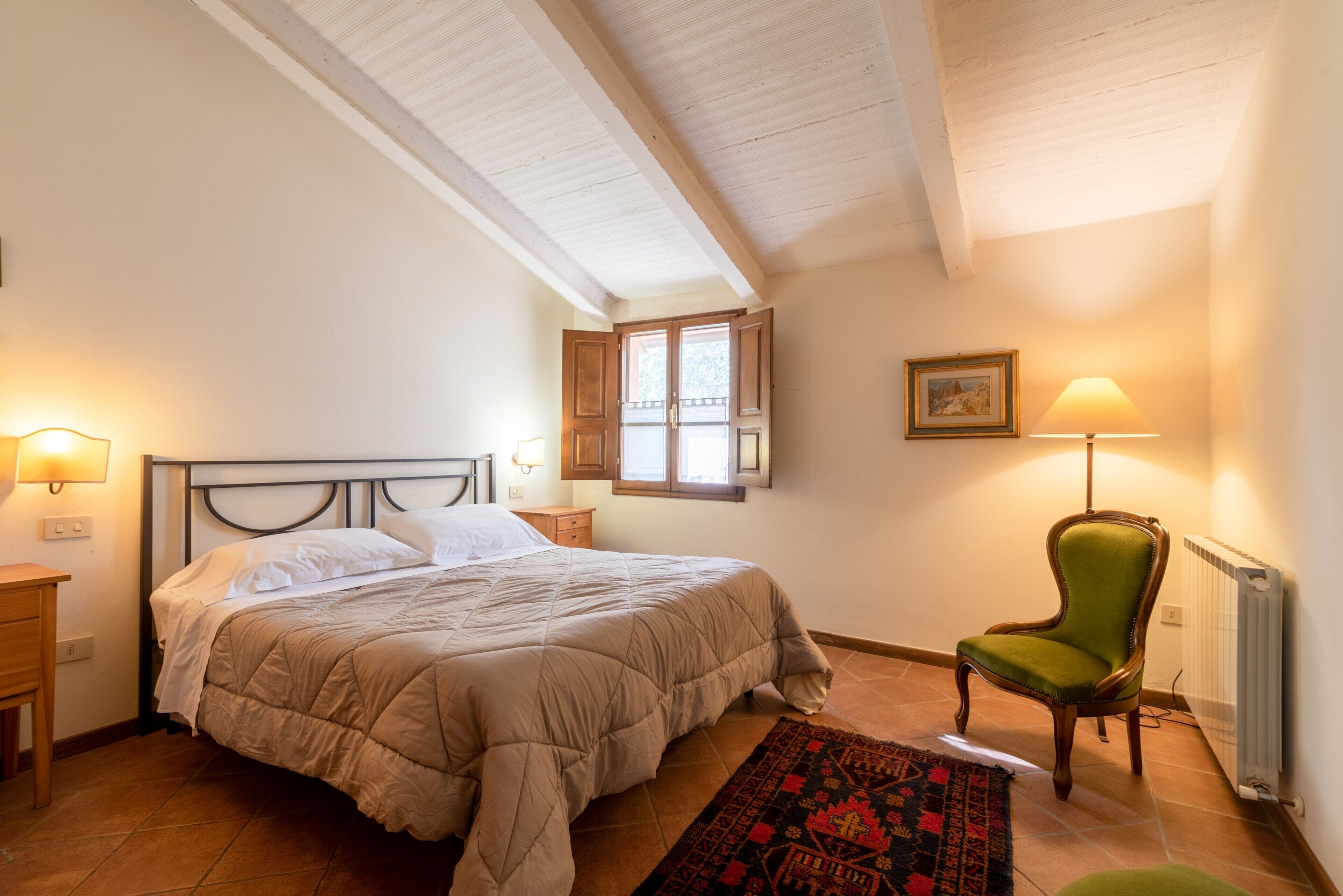 Een slaapkamer met een bed, een stoel, een raam en een lamp.