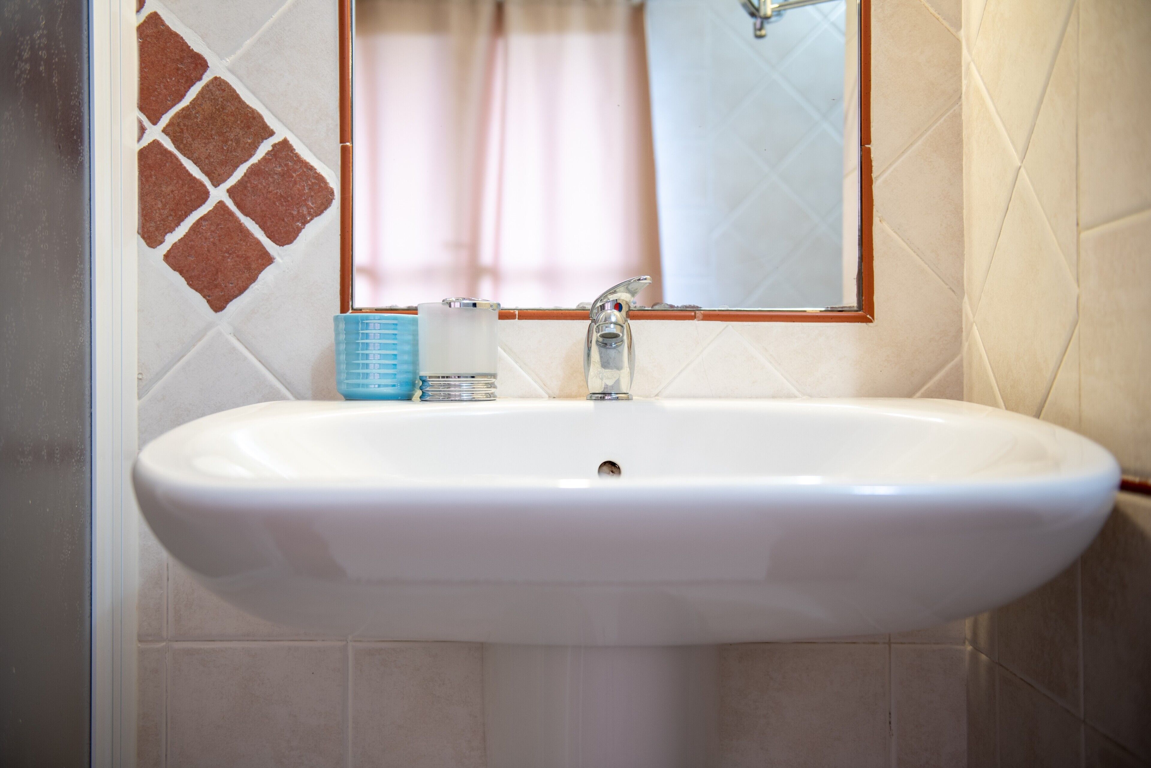 A bathroom with a white sink, a mirror, and a tiled wall.