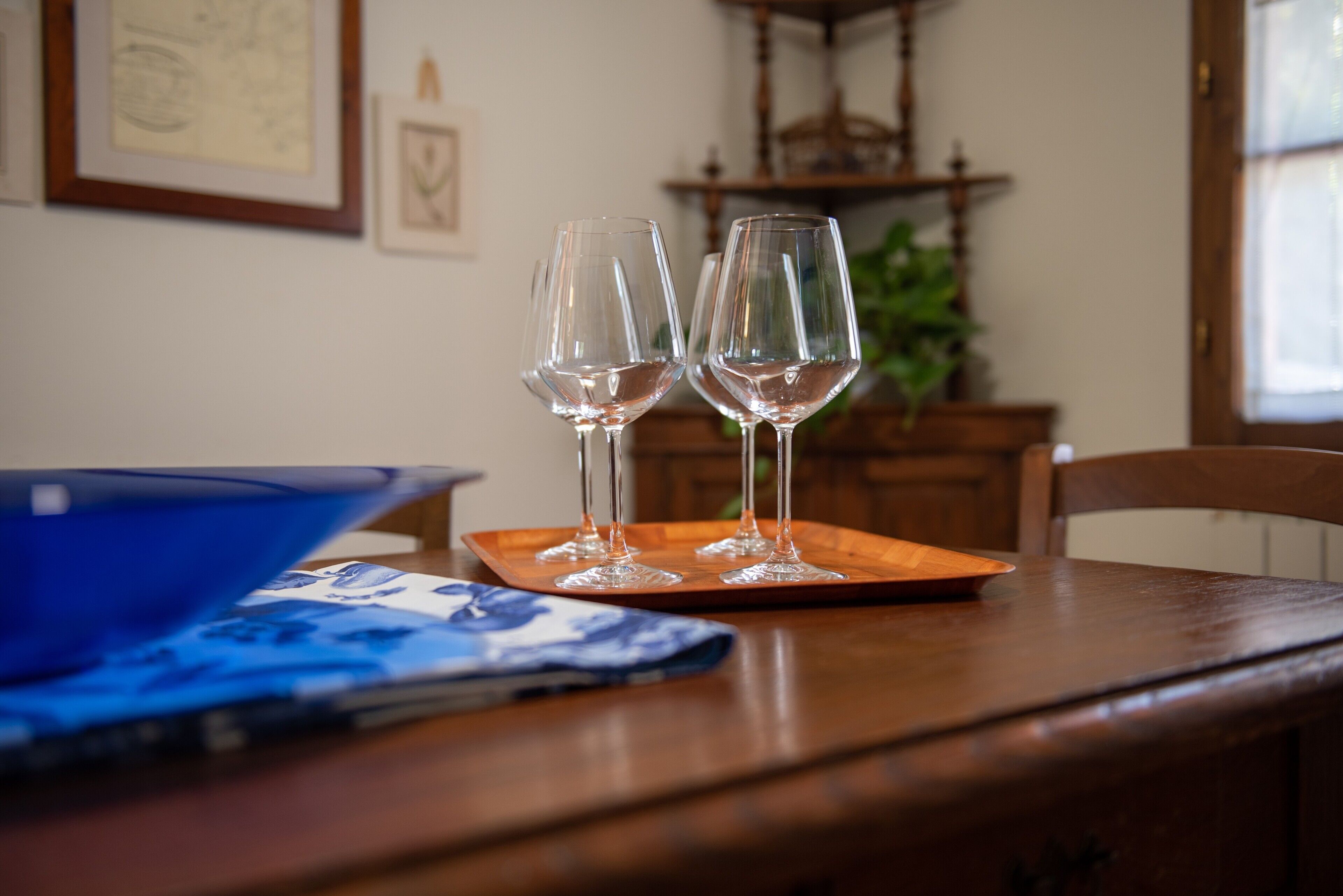 A dining table with two wine glasses on a tray, a blue bowl, and a blue and white patterned napkin.