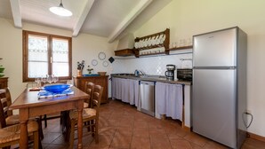 Une cuisine équipée d’une table à manger, de chaises, d’un réfrigérateur et d’une fenêtre avec des stores.