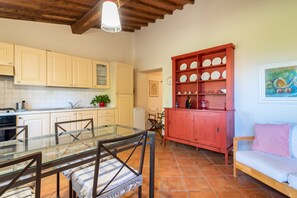 Una cocina con armarios de madera, una mesa de comedor de vidrio y un aparador rojo con vajilla.