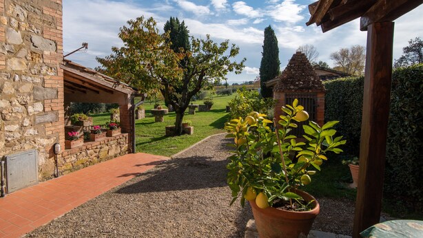 Un sentier de jardin mène à un bâtiment en pierre, doté d’un mur en briques, d’une pergola et d’une petite construction en briques en arrière-plan.