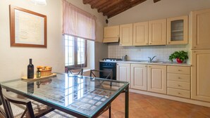 Une cuisine avec une table à plateau en verre, des chaises en bois, une cuisinière, des placards et une fenêtre avec des rideaux.