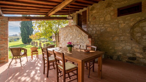 A covered patio with a wooden table and chairs, stone walls, and a view of a garden. - Villa 'Il Fienile Il Sole Verde' with Shared Pool and Wi-Fi (Bucine)