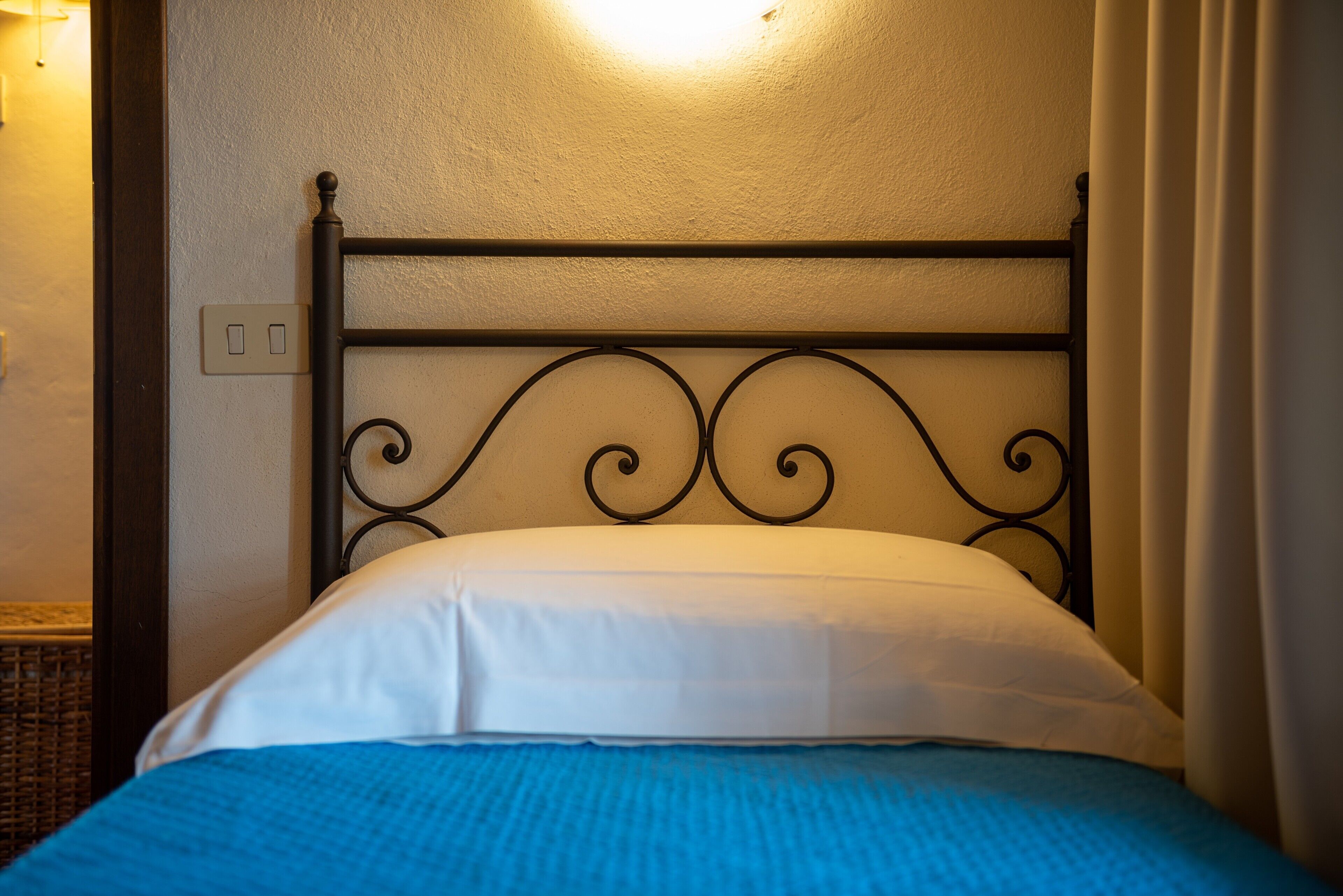 Un lit avec une tête de lit en métal, un oreiller blanc et une couverture bleue.