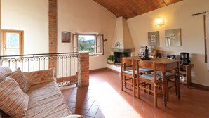 A cozy living room with a sofa, dining table, chairs, a fireplace, and a balcony with a railing. - Villa 'Il Fienile Il Sole Verde' with Shared Pool and Wi-Fi (Bucine)