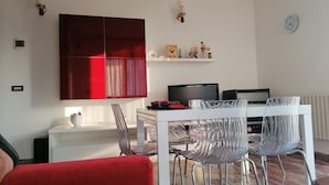 A modern living room with a red sectional sofa, a white dining table with clear chairs, a flat-screen TV, and a mounted shelf with decorative items. - Pet-Friendly Apartment 'Casa Rosciano' with Mountain View & Garden (rosciano)