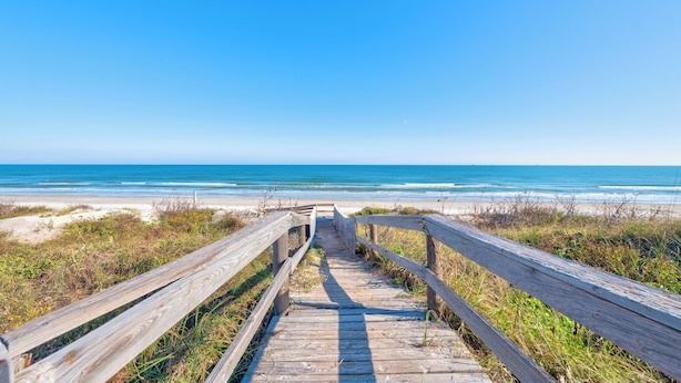 A wooden boardwalk leading to a beach with clear skies.