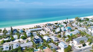 An aerial view of a coastal residential area with houses, a beach, and clear blue waters.
