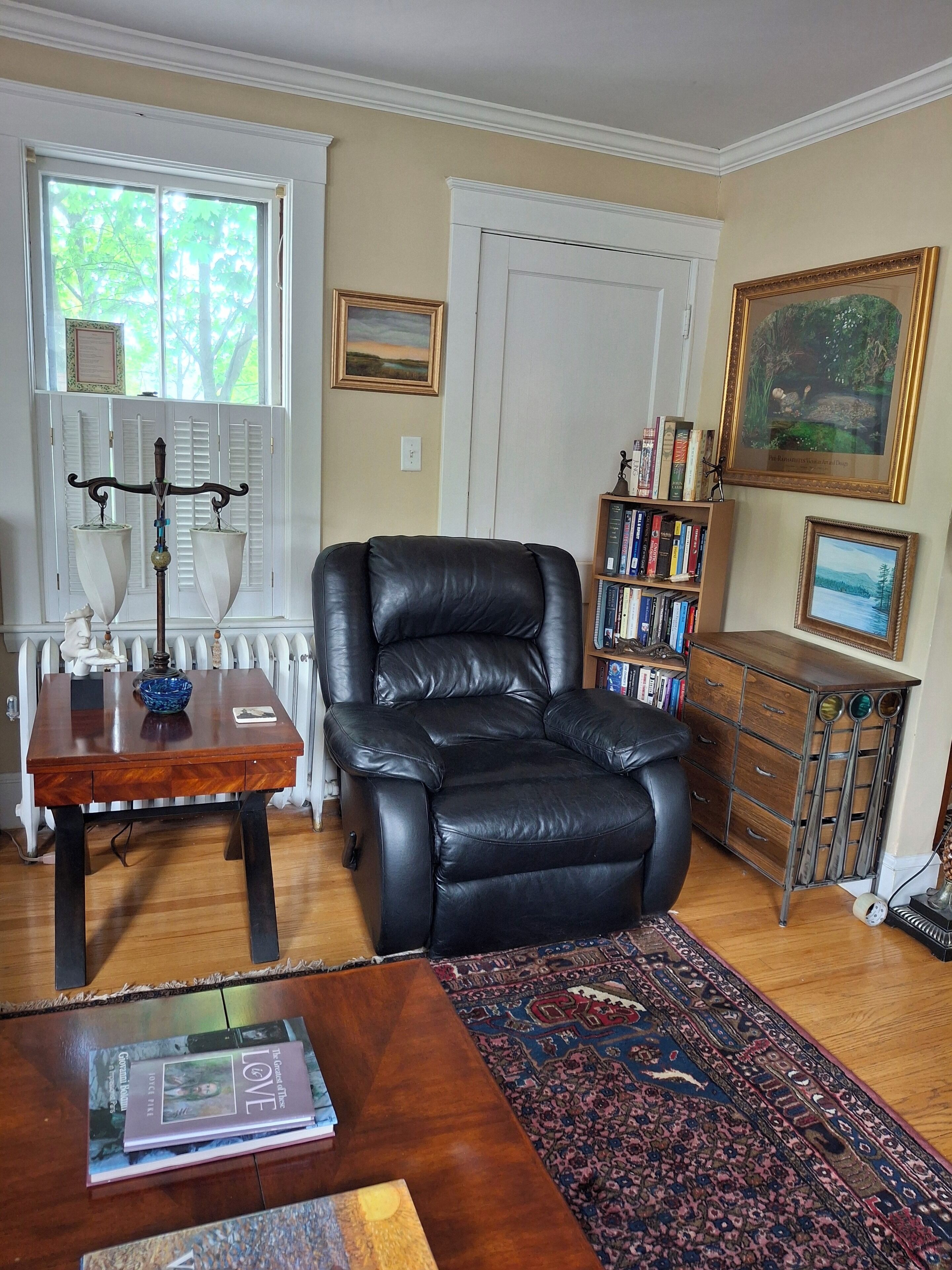 A living room with a black leather chair, a wooden coffee table, a bookshelf, and a patterned rug.