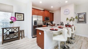 A modern kitchen with stainless steel appliances, a wooden island, and a dining area with white bar stools. - Last Minute Disney Getaway! Townhouse with Private Pool. Book Now! #17058 (Orlando)