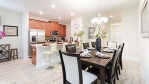 A modern kitchen with stainless steel appliances, a dining area with a large table and chairs, and a chandelier. - Last Minute Disney Getaway! Townhouse with Private Pool. Book Now! #17058 (Orlando)