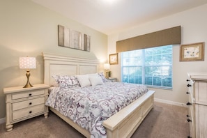 Quarto com cama, mesas de cabeceira, cômoda e janela com persianas.