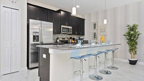 A modern kitchen with dark cabinets, stainless steel appliances, a granite countertop, and bar stools.