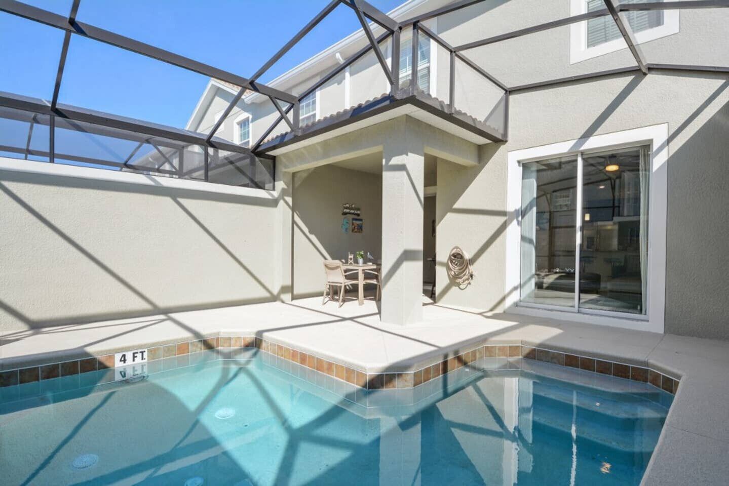 A swimming pool with a glass enclosure, a patio area with a table and chairs, and a covered outdoor seating area.