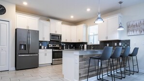 A modern kitchen with white cabinets, stainless steel appliances, and a central island with bar stools.