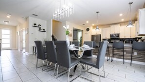 A modern kitchen with stainless steel appliances, a dining area with a glass table and black chairs, and a chandelier.
