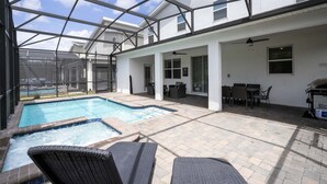 A covered outdoor pool area with lounge chairs, a hot tub, and a patio with tables and chairs.