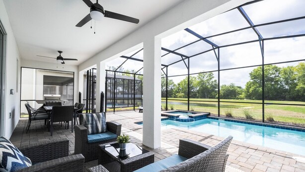 A covered outdoor area with a pool, wicker furniture, ceiling fans, and a view of the outdoors.