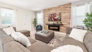 A modern living room with a fireplace, grey sofas, and a large wall-mounted TV.