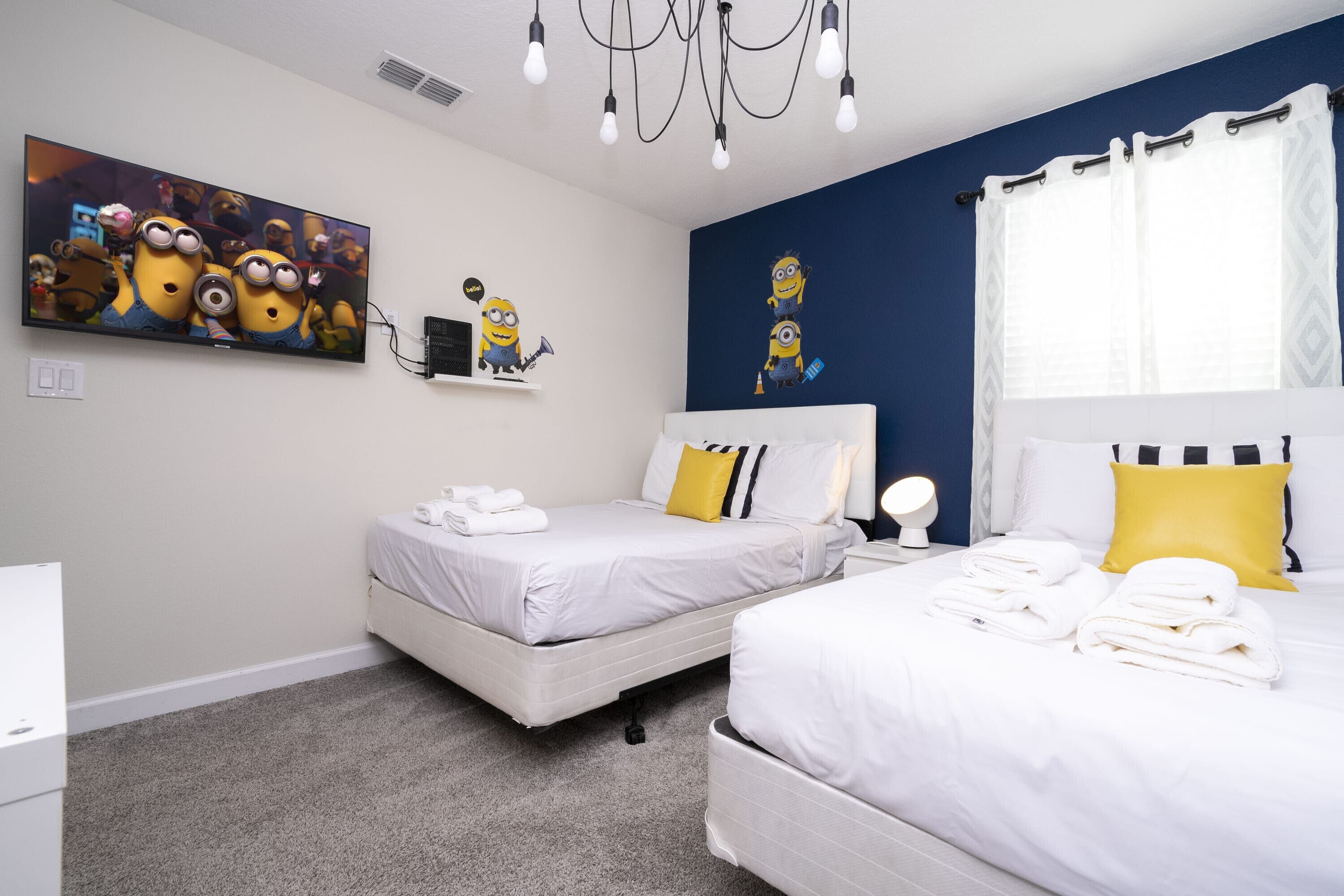 A hotel room with two beds, a large TV on the wall, and a Minion-themed decoration.