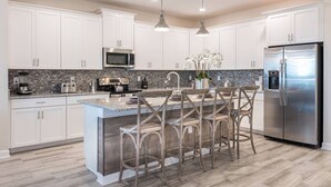 A modern kitchen with white cabinets, a stainless steel refrigerator, a built-in microwave, and a granite countertop.