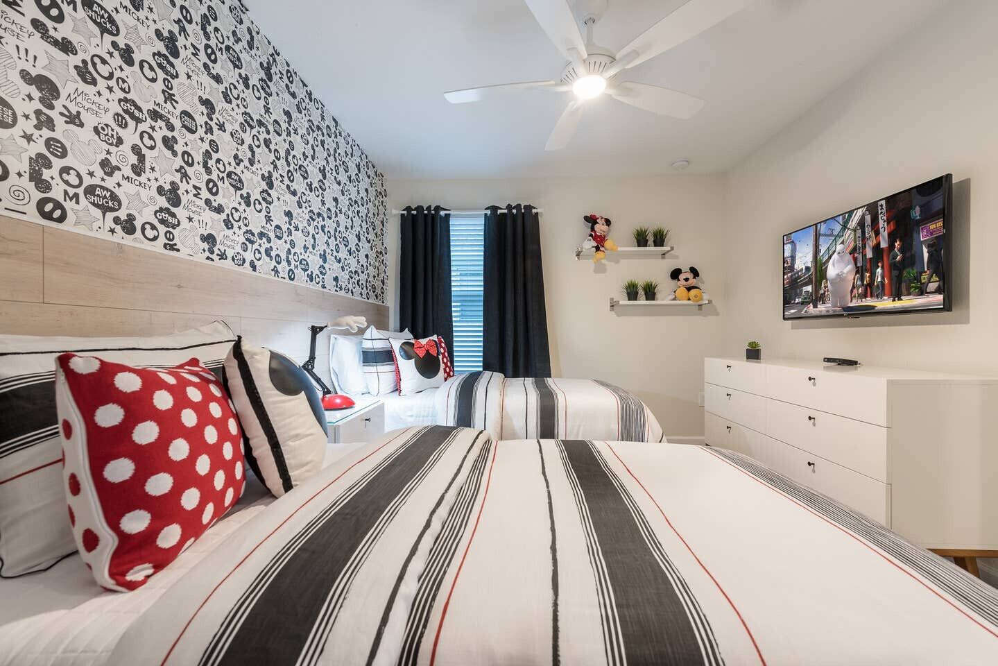 A bedroom with a bed, a dresser, a ceiling fan, a TV, and a Mickey Mouse statue.