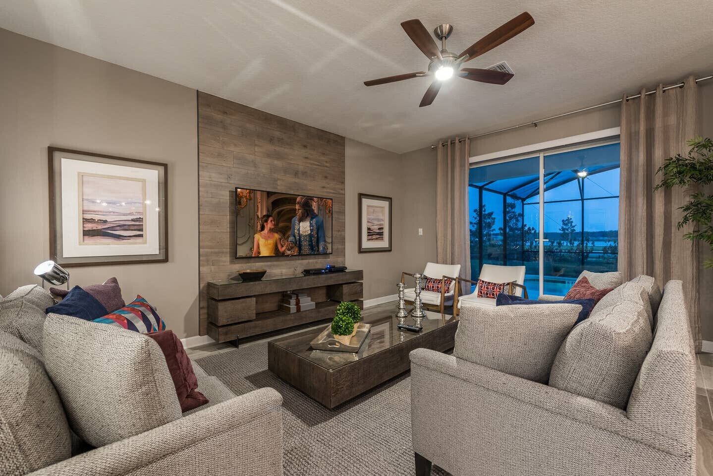 A modern living room with a flat-screen TV, comfortable seating, a coffee table, and a large window with a view.