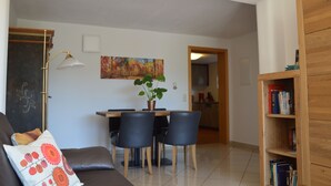 Una sala de estar con sofá, una mesa de centro y un comedor con sillas y una mesa. Hay una estantería y un cuadro en la pared.