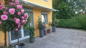 Un edificio amarillo con camino pavimentado, plantas en macetas y un pequeño banco de ladrillo.