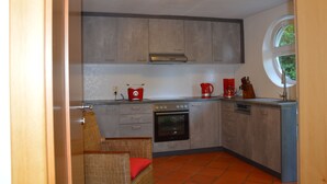 Una cocina compacta con armarios grises, horno integrado y hervidor rojo.