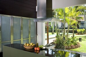 A modern kitchen with a glass-top island, a bowl of fruit, and a small garden view.