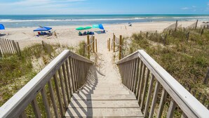 Una escalera de madera que lleva a una playa con sombrillas y sillas de playa.