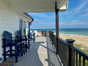 A wooden deck with blue Adirondack chairs, a wooden table, and a view of the beach and ocean. - Wynd Swept # 111 Oceanfront House, Pool, Tennis courts, kayak launch! (North Topsail Beach)