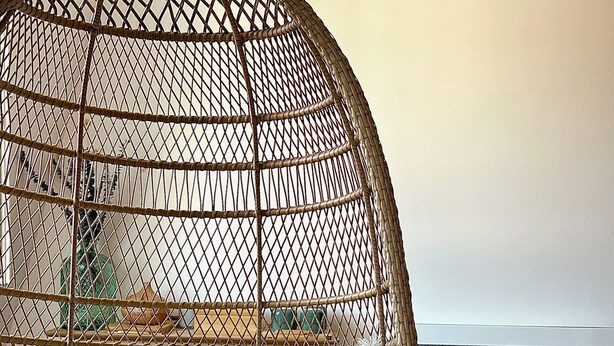 A hanging chair with a woven frame and white cushions, wooden blocks, and a woven light fixture in a room with a carpeted floor. - Le Verdoyant *** (Colmar)