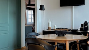 A modern dining area with a wooden table, black chairs, a mounted TV, and a unique ceiling light fixture. - Le Verdoyant *** (Colmar)