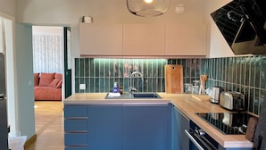 A modern kitchen with a central island, a sink, and a stove. There are cabinets above the sink and a backsplash with green tiles. - Le Verdoyant *** (Colmar)
