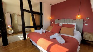 A bedroom with a large bed, wooden beams, a red wall, and two pendant lights. - Le Verdoyant *** (Colmar)