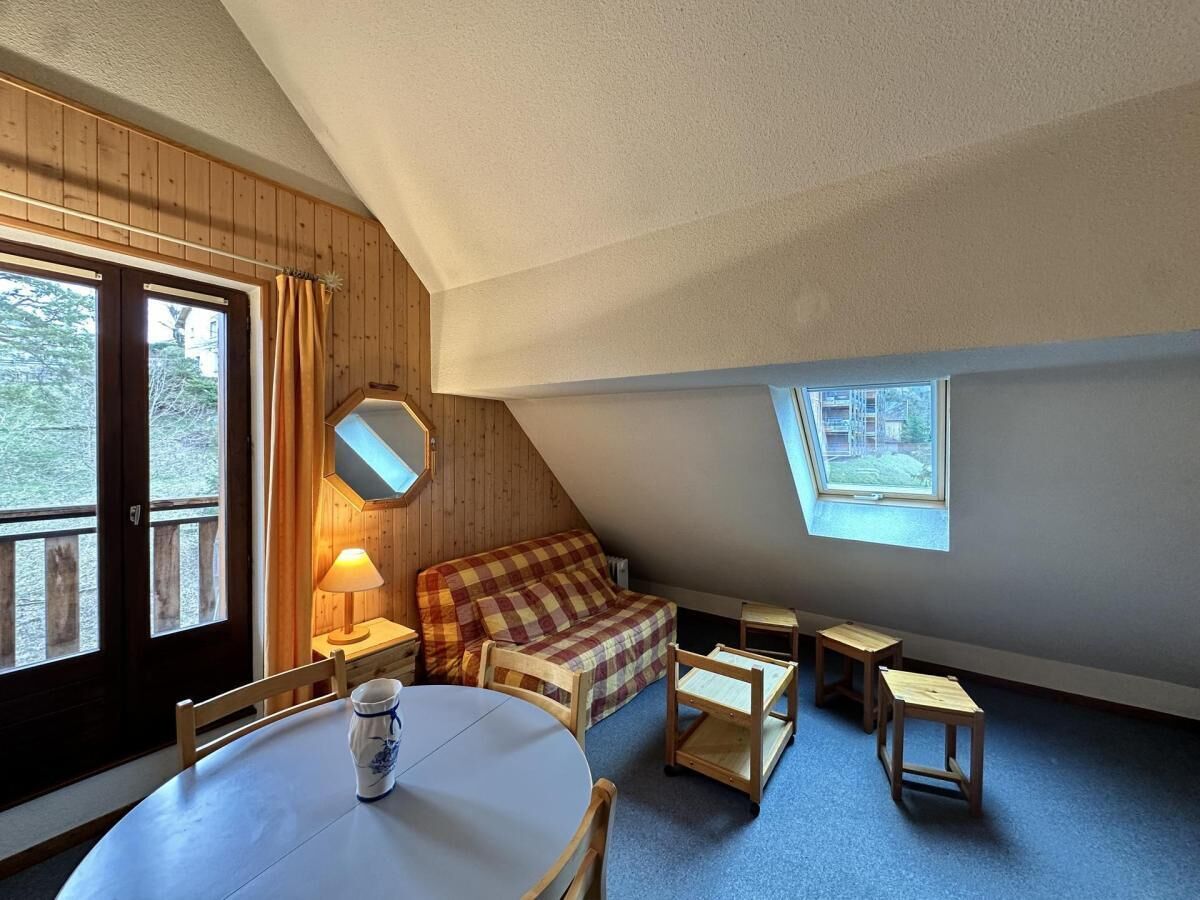 Een gezellige slaapkamer onder de dakpannen met een geruit bed, een ronde tafel en een kleine lamp.