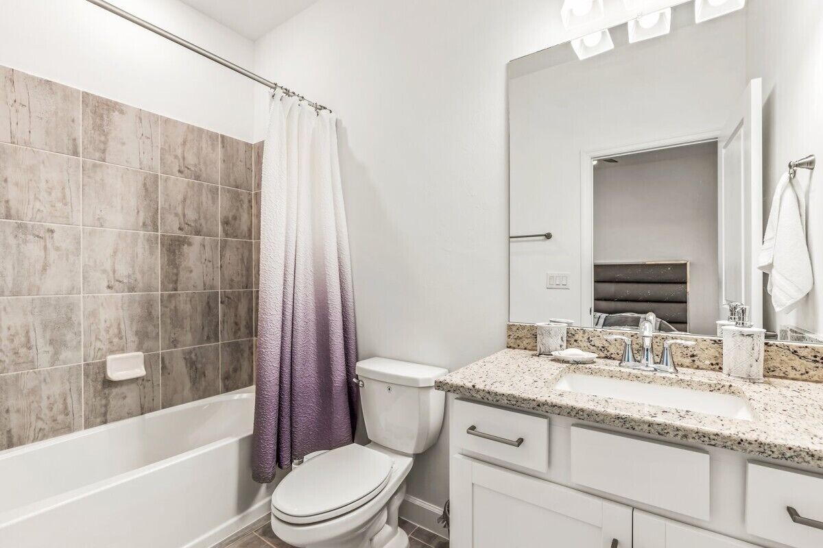 Un baño con bañera, inodoro y tocador con lavamanos y espejo.