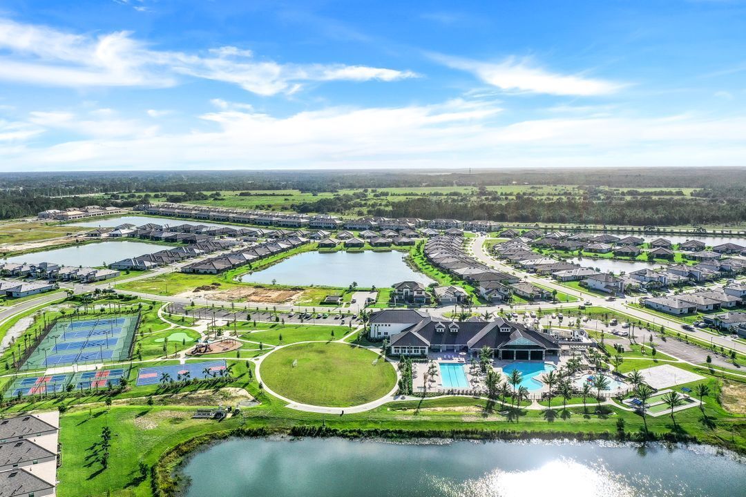 Vue aérienne d’un complexe résidentiel comprenant plusieurs logements, une piscine centrale, des courts de tennis et un grand lac.