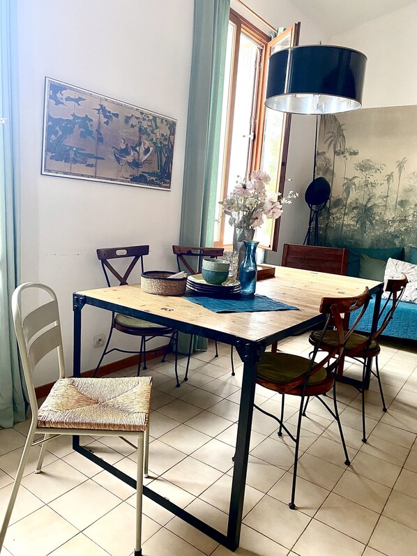 A dining area with a wooden table, chairs, a vase with flowers, and a wall-mounted painting.