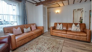 Uma sala de estar com dois sofás de couro marrom, um tapete estampado e vigas de madeira no teto.