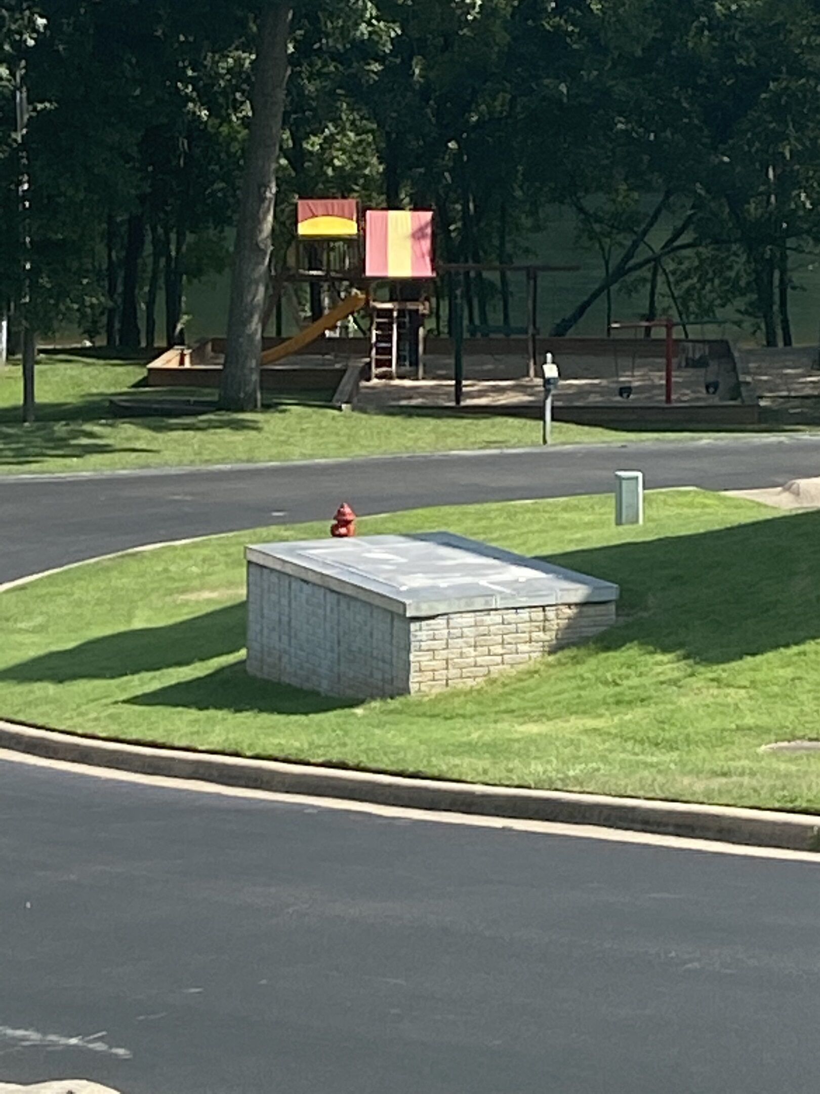 Un parque con un parque infantil, un hidrante y una pequeña construcción de ladrillo.