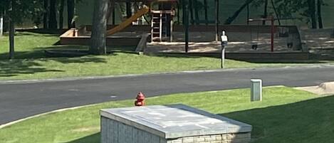 Un parque con un parque infantil, un hidrante y una pequeña construcción de ladrillo.