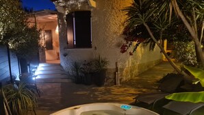 A hot tub in a courtyard with a stone wall, potted plants, and a staircase leading to a door.