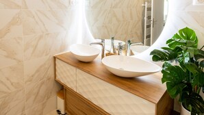 A bathroom with two white vessel sinks, a wooden vanity, a large mirror, and a potted plant.