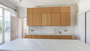 A modern kitchen with a large marble countertop, wooden cabinets, and a built-in sink. - Appartement Haussmannien D'exception Coeur de Paris (Paris)