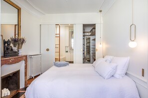 Quarto com uma cama grande, cômoda, espelho e radiador.